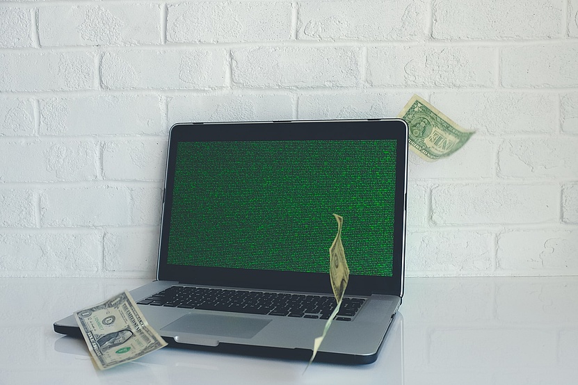 Laptop mit grünem Bildschirm. Rundherum fliegen Geldnoten.
